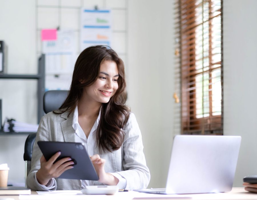 Asian Business woman using calculator and laptop for doing math finance on an office desk, tax, report, accounting, statistics, and analytical research concept.
